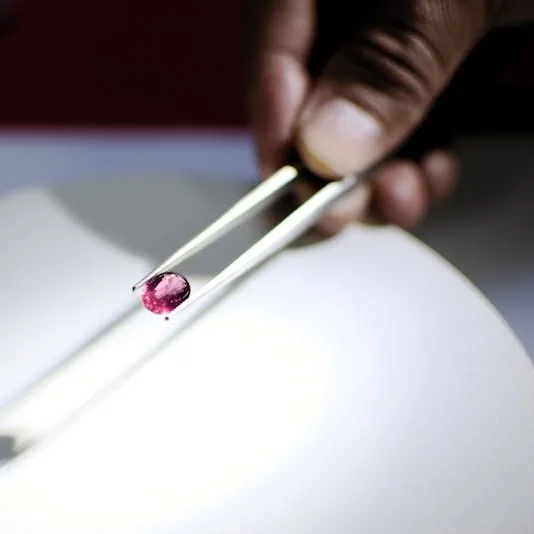 A faceted pink gemstone held in tweezers over a lamp in the reference collection