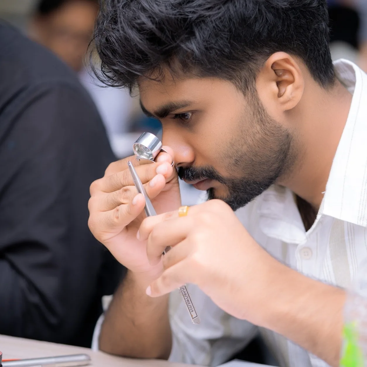 A student examining a gemstone through a jeweller's loupe during a practical class